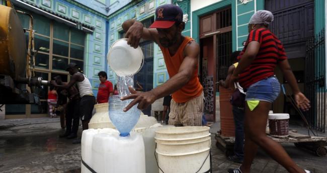Cubanos llenan vasijas con una pipa de agua.