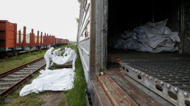 Militares ucranianos llevan los cuerpos de soldados rusos muertos a un vagón refrigerado, en Kiev, Ucrania, el 13 de mayo de 2022. 