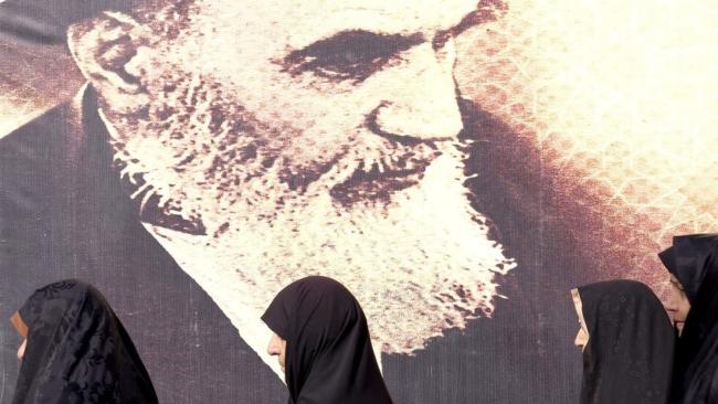 Mujeres pasan junto a una imagen del ayatola Ruhollah Jomeini.