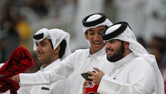 Qataríes miran un celular en un estadio de fútbol.
