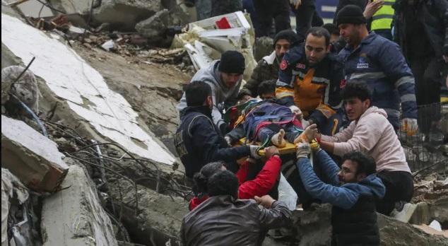 Gente y equipos de rescatistas trasladan a una persona en camilla desde un edificio derruido en Adana, Turquía.
