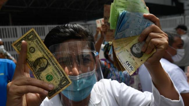 Un venezolano con un dólar en una mano y bolívares en la otra.