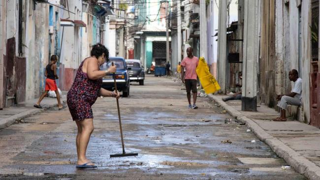 Una mujer barre una calle en Cuba.