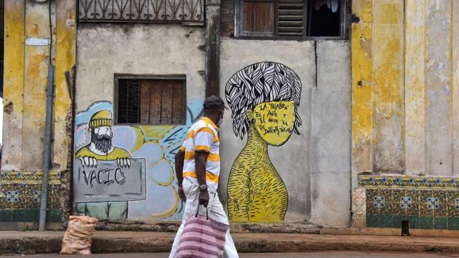 Un hombre cruza ante dos grafitis en una calle de La Habana.