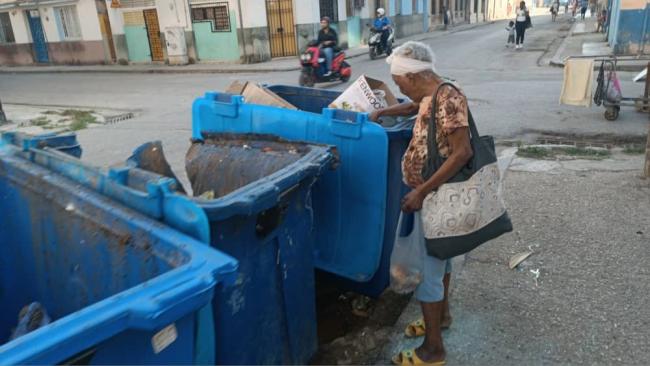 Una mujer revisando un contenedor de basura en Cuba.