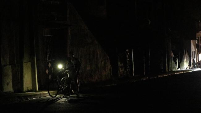 Cubanos se iluminan con la linterna de un teléfono en una calle oscura.