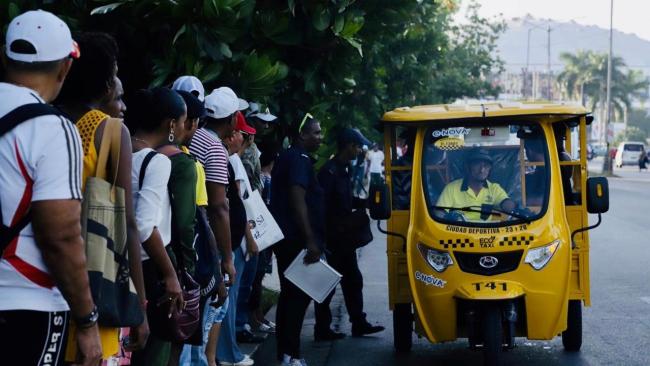 Cubanos hacen cola para montarse en un triciclo eléctrico en La Habana.