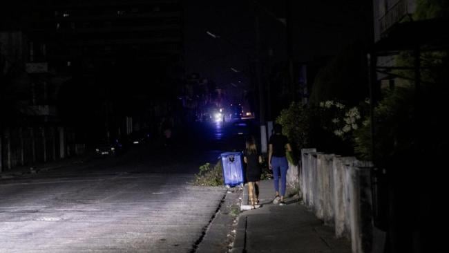 Dos jóvenes caminan por una acera de La Habana a oscuras.