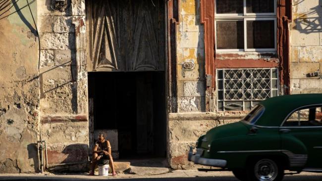 Una mujer sentada a la entrada de una edificación en La Habana.