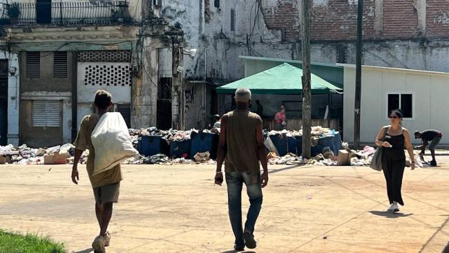 Personas caminan cerca de un basurero en La Habana.