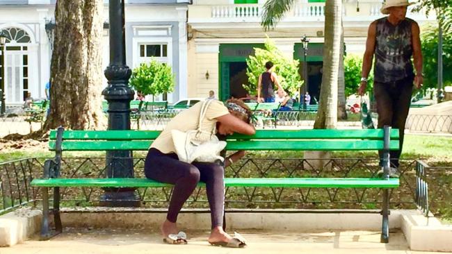 Mujer cubana exhausta en un banco en La Habana.