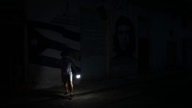 Un hombre se alumbra con una lámpara en una calle de La Habana a oscuras.