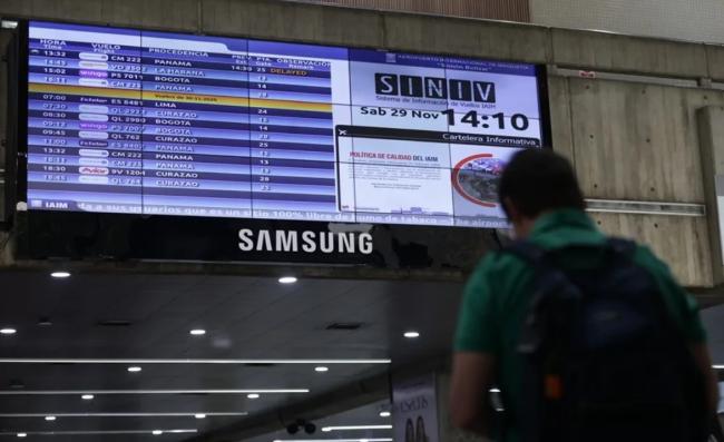 Una persona camina junto a una pantalla con información de vuelos, en el Aeropuerto Internacional Simón Bolívar.