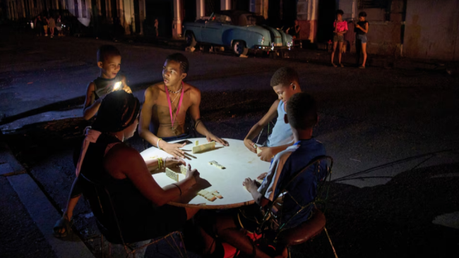Cubanos juegan dominó con la linterna de un teléfono durante un apagón.