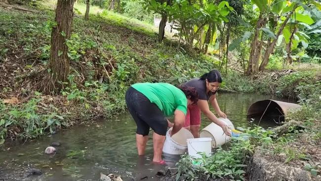 Mujeres cargan agua desde un río para llevar a su vivienda.
