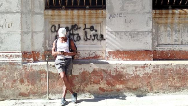 Un hombre recostado sobre una pared con una pintada contra el régimen.