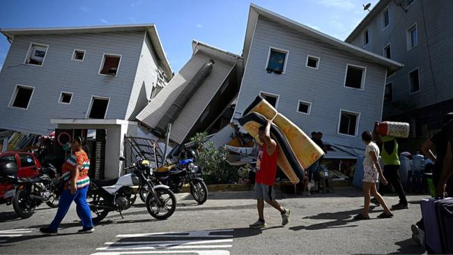 Un hombre carga un colchón frente a edificios dañados por los terremotos.