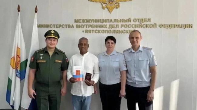 El cubano acompañado por funcionarios durante el acto de entrega del pasaporte ruso.