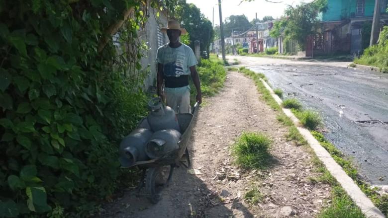 Un hombre lleva tres balitas de gas en una carretilla.