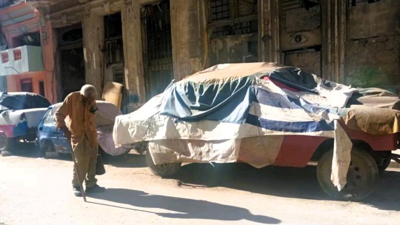 Una anciano y carros antiguos en una calle de La Habana.